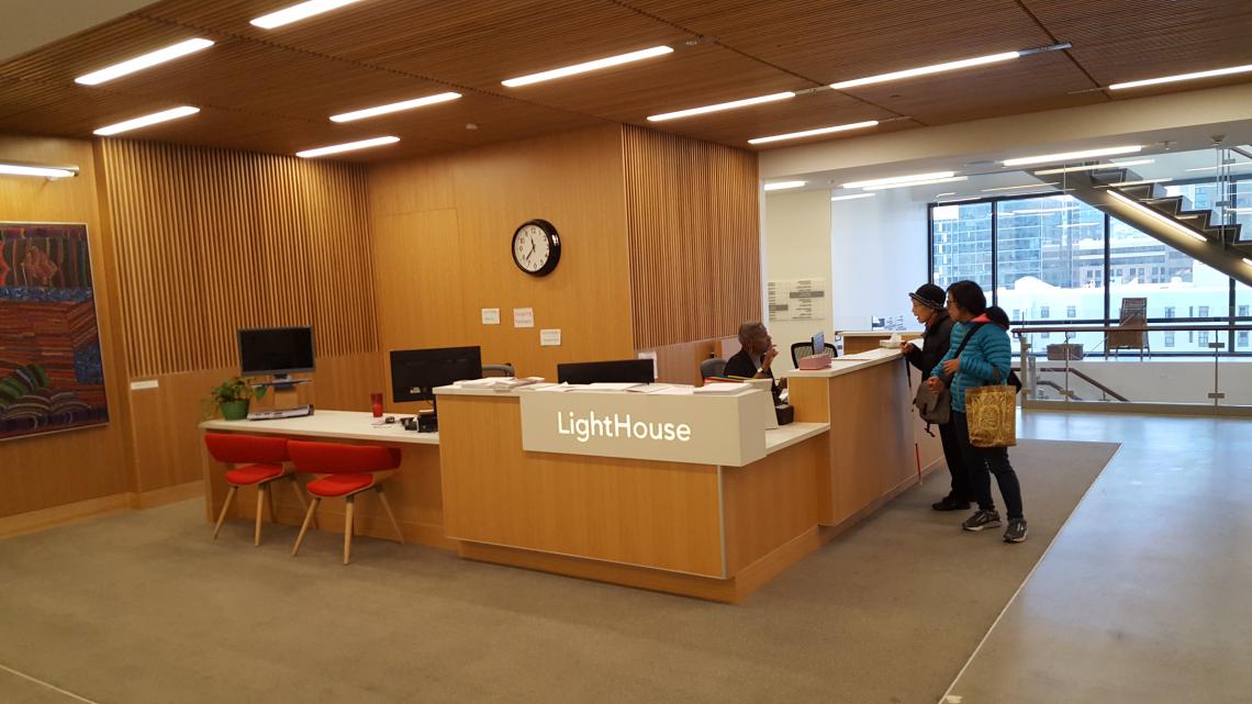2 people speaking to the receptionist at the front desk in the main lobby of the Lighthouse for the Blind in San Francisco